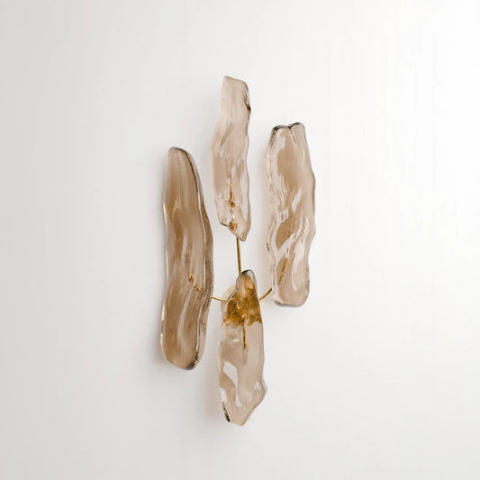Product view of Antony Gasnier’s Pinaster wall lamp with four irregular amber glass diffusers arranged on a brass structure.