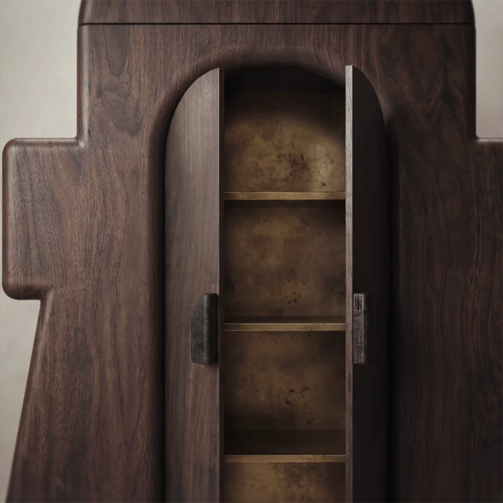 Close-up of the open Le Gardien cabinet, revealing brass-toned interior panels and shelves framed by dark wood doors.
