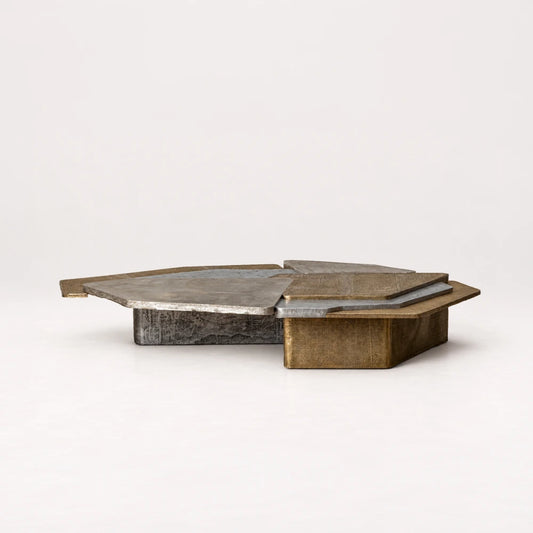 Low side view of the Scorpio 240 Coffee Table by Eva Szumilas, showing layered metallic surfaces above broad gold-toned and silver-toned bases.