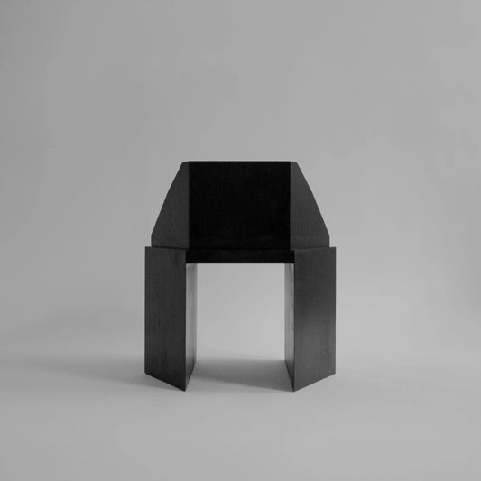 Front view of the black Ana Chair by Sizar Alexis, featuring a wide seat, sloping armrests, and open architectural base.