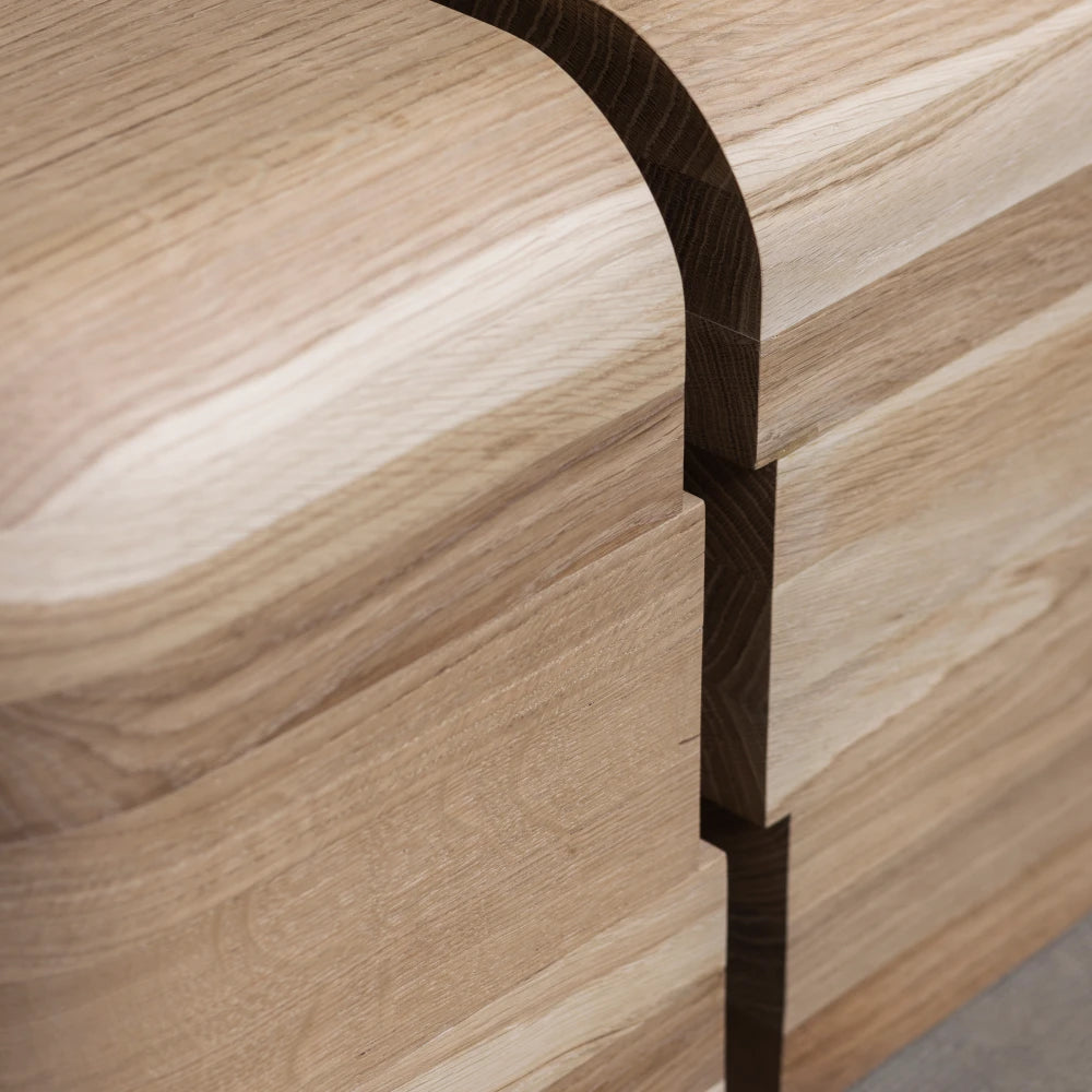Close-up of the Lahmu Stool Natural by Sizar Alexis, highlighting curved oak grain, layered construction, and precise dark joinery.