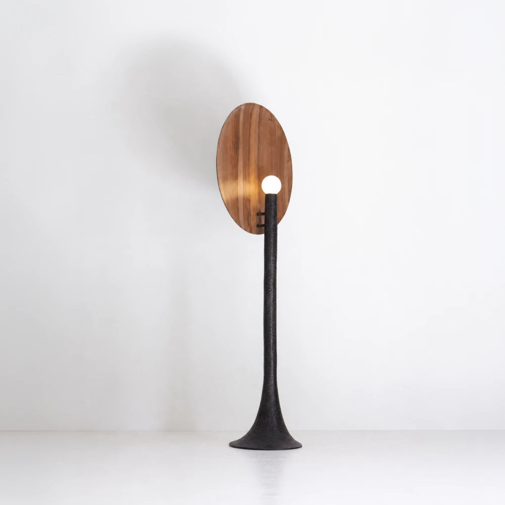 Rear three-quarter view of the illuminated Solis floor lamp, with a glowing sphere set against the walnut disc
