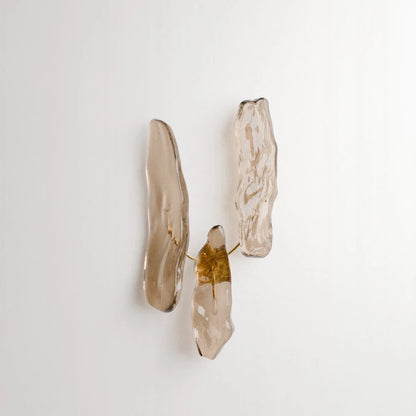 Front view of Antony Gasnier’s Pinaster wall lamp, featuring three irregular amber glass diffusers arranged around a brass structure.