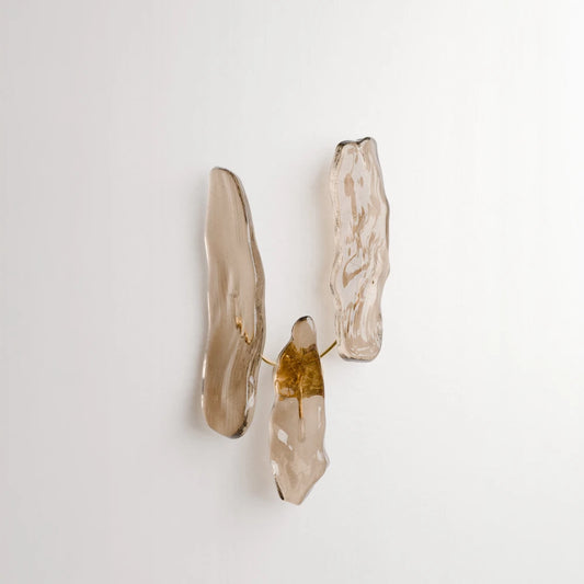 Front view of Antony Gasnier’s Pinaster wall lamp, featuring three irregular amber glass diffusers arranged around a brass structure.
