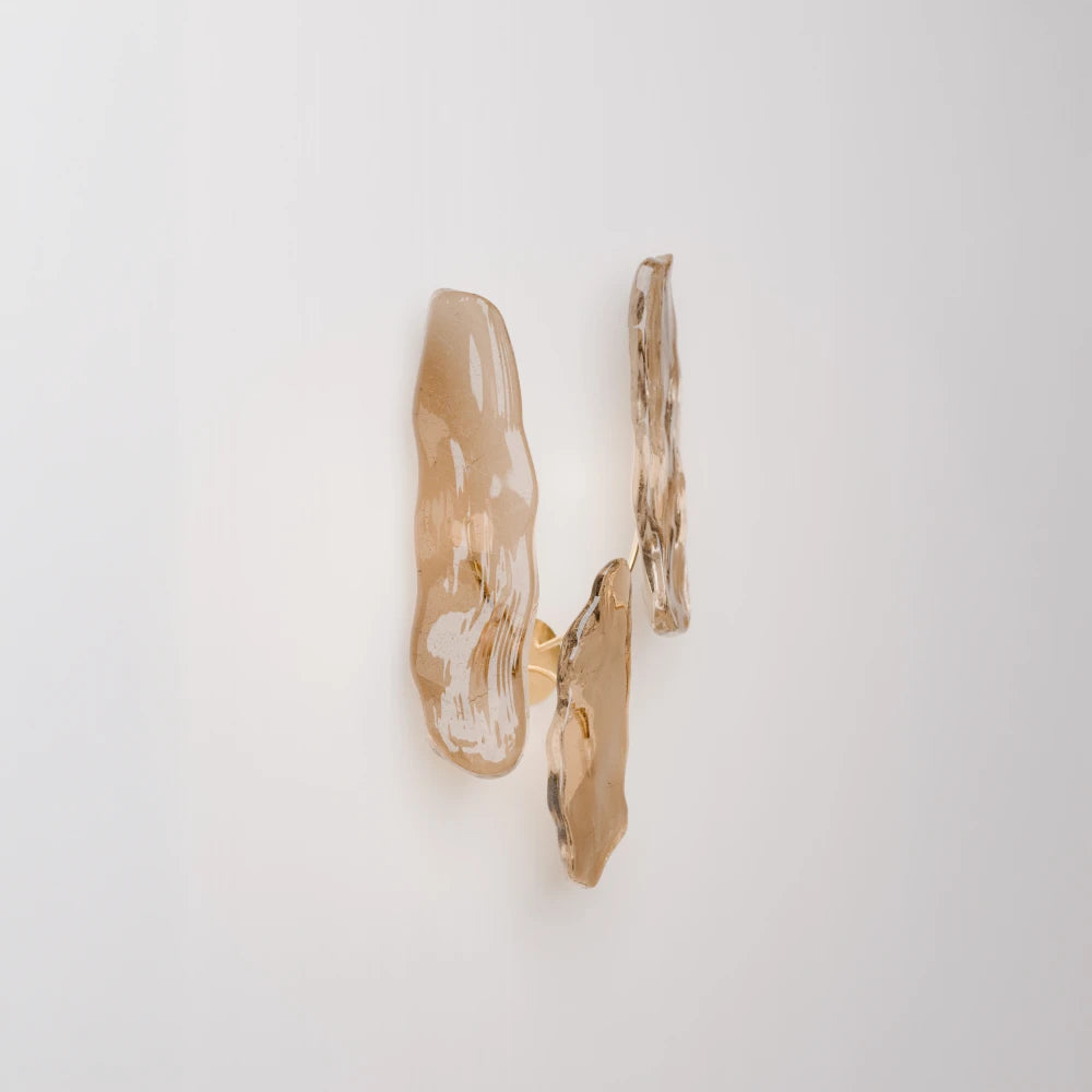 Angled view of the Pinaster three-source wall lamp by Antony Gasnier, softly illuminated through sculptural amber glass diffusers.