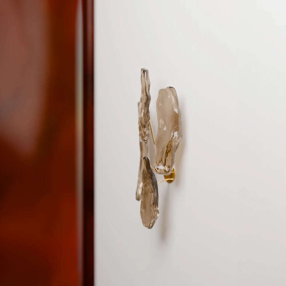 Side view of the Pinaster wall lamp by Antony Gasnier installed on a white wall beside a dark wood panel.