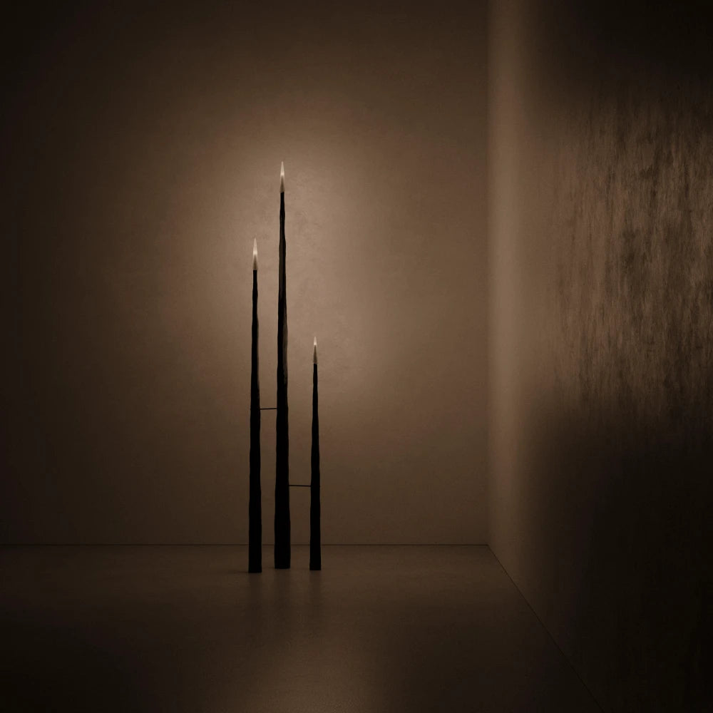 Three illuminated Winter Candle holders in blackened wood by Antony Gasnier displayed in a dark interior