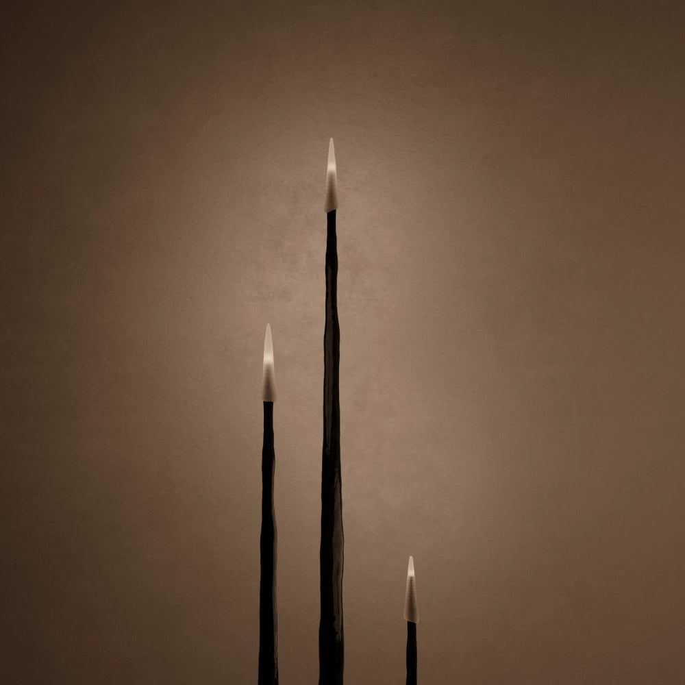 Close-up of the glowing tapered candles and sculpted black wood stems of the Winter Candle set by Antony Gasnier