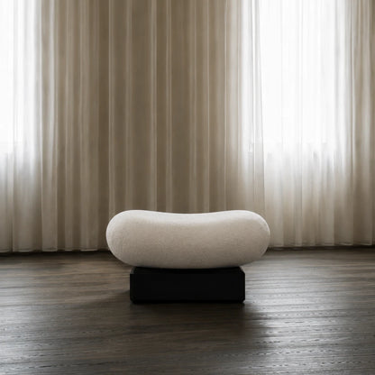 Winter Ottoman by Antony Gasnier displayed alone on a dark wood floor beside sheer curtains