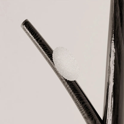 Close-up of a textured glass diffuser mounted on the dark wood branch of Antony Gasnier’s Winter Tree Light floor lamp.