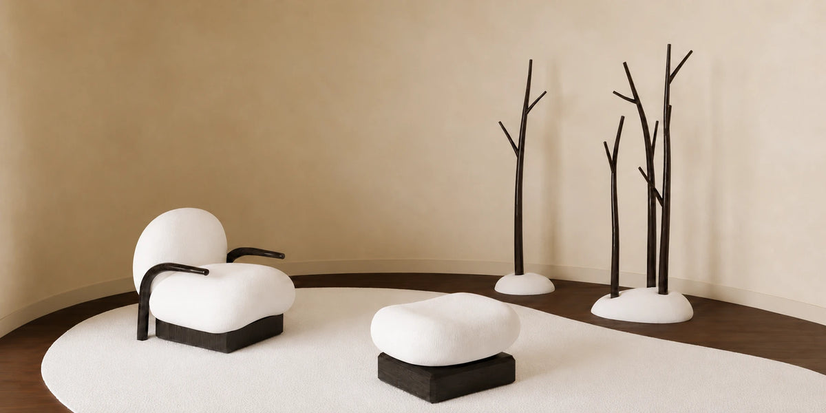 Winter Collection by Antony Gasnier, featuring a white upholstered armchair and ottoman with dark wooden bases, alongside sculptural tree-shaped coat stands in a warm interior. Represented by Lythore