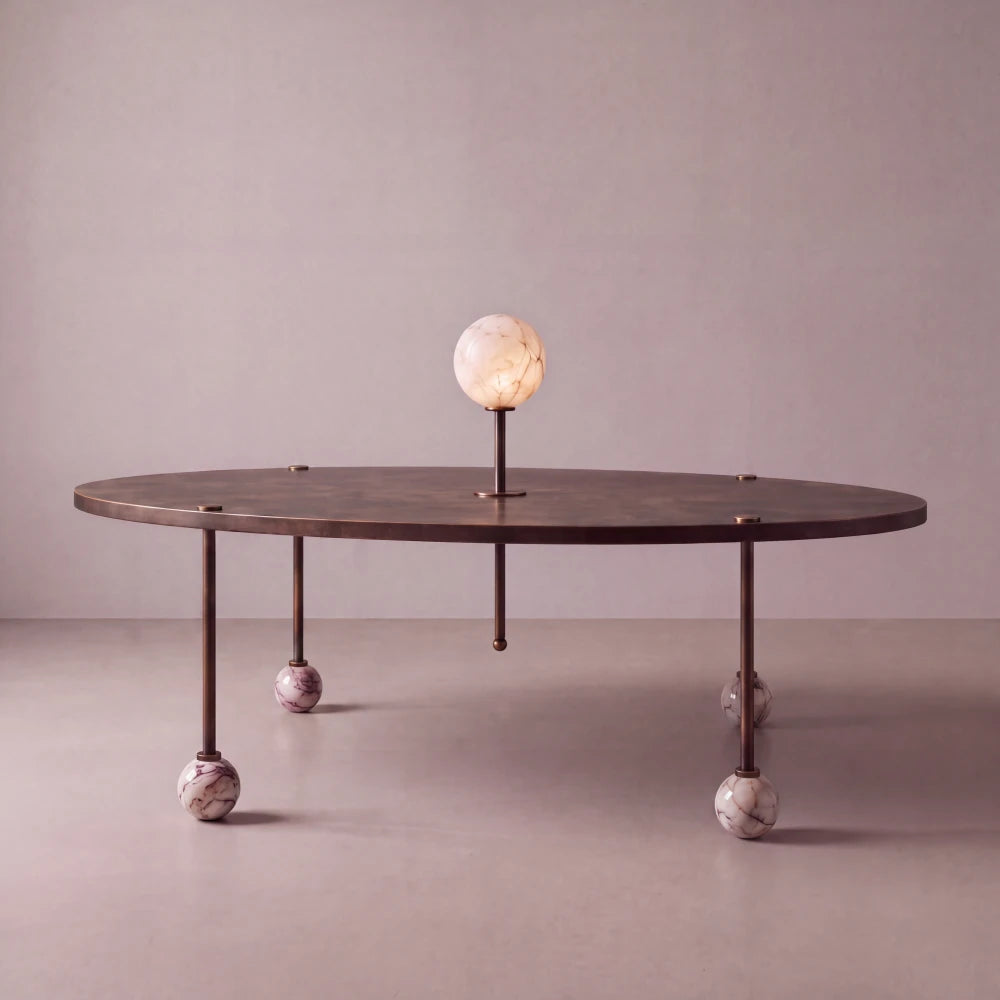 Front view of the Ballet dining table by Diamant Versatile, with an oval bronze-toned top, veined marble ball feet and luminous stone centerpiece.