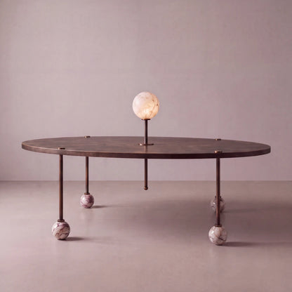 Front view of the Ballet dining table by Diamant Versatile, with an oval bronze-toned top, veined marble ball feet and luminous stone centerpiece.