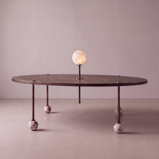 Front view of the Ballet dining table by Diamant Versatile, with an oval bronze-toned top, veined marble ball feet and luminous stone centerpiece.