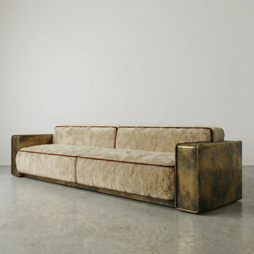 Three-quarter view of the Peau Sofa by Diamant Versatile, showing its low silhouette, cream upholstery and patinated gold-toned metal frame.