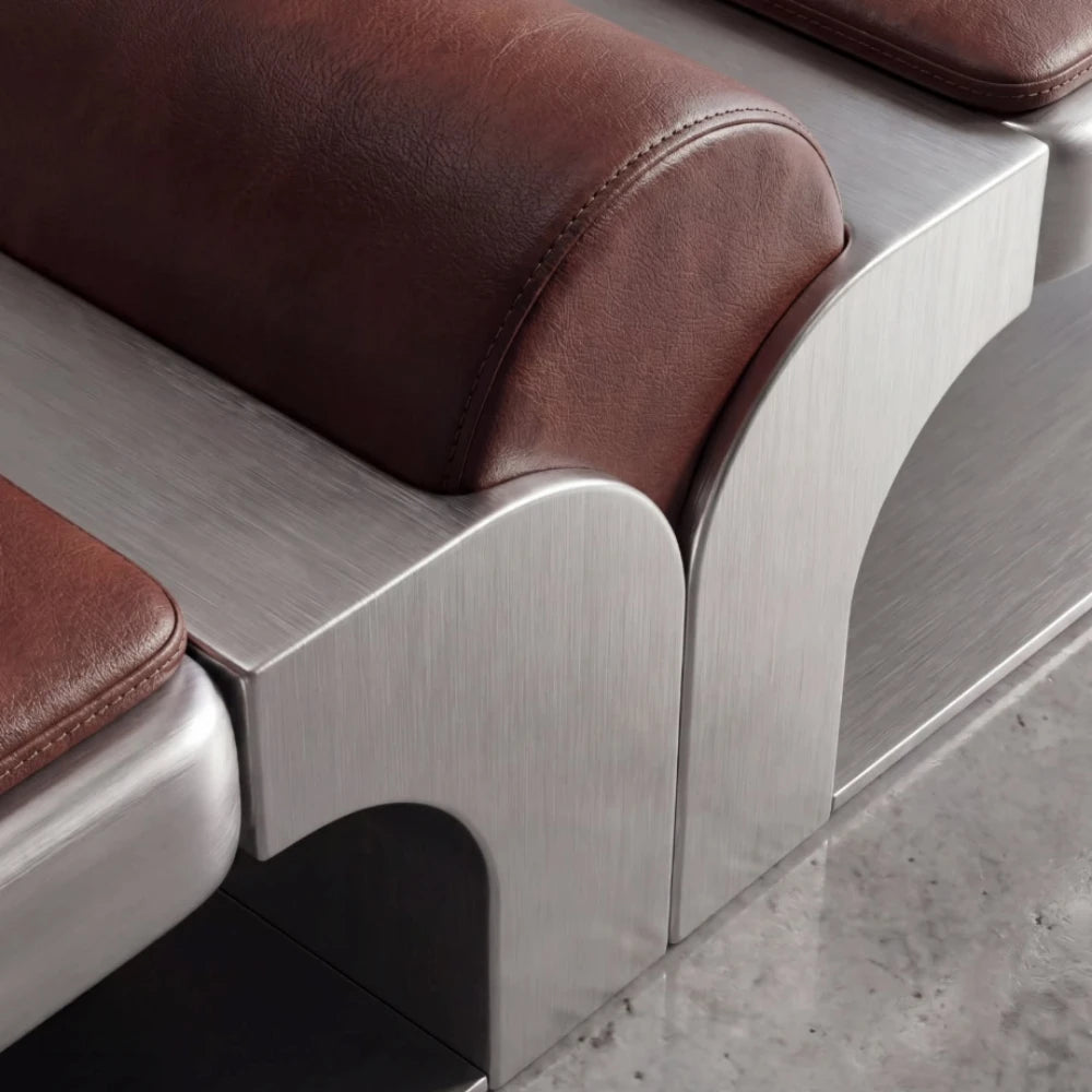 Close-up of the Confluence bench showing the stitched brown leather centre cushion and curved brushed metal structure.