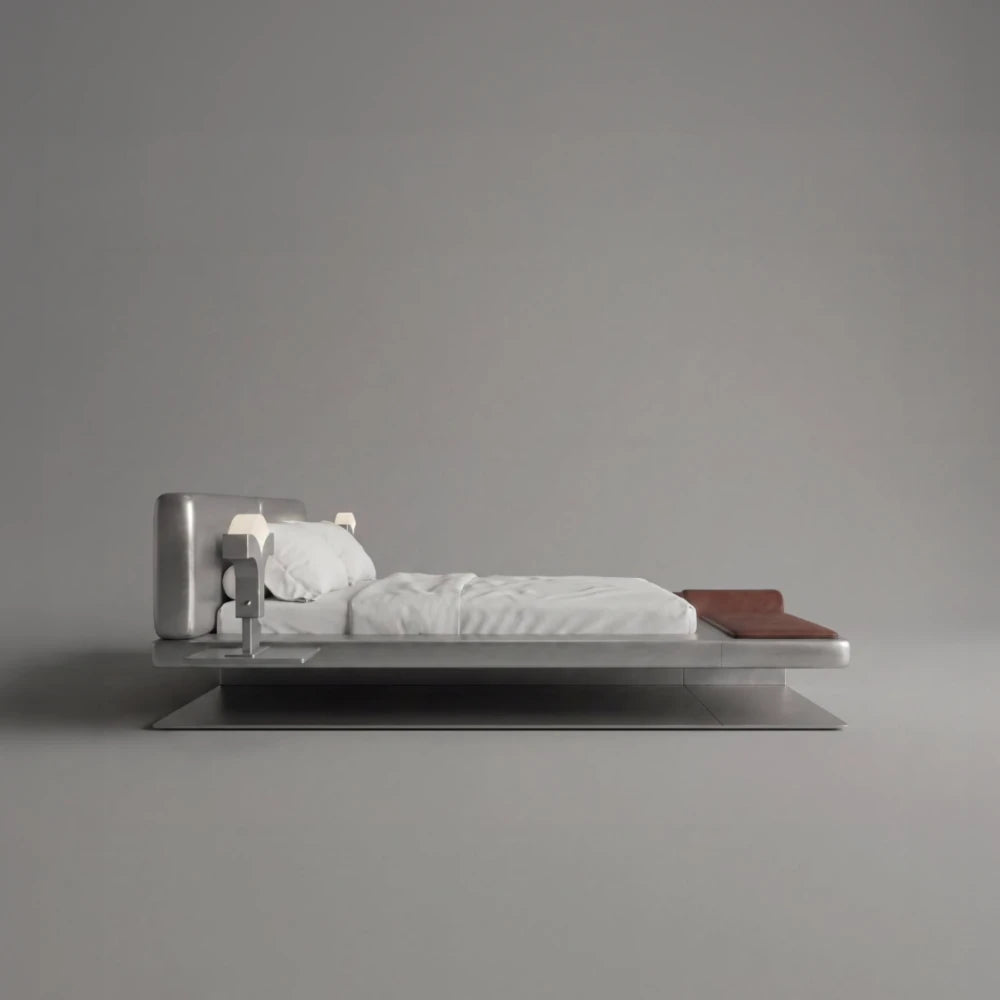 Side view of the Confluence bed by Diamant Versatile, with white bedding, brown leather details and a sculptural brushed metal frame.