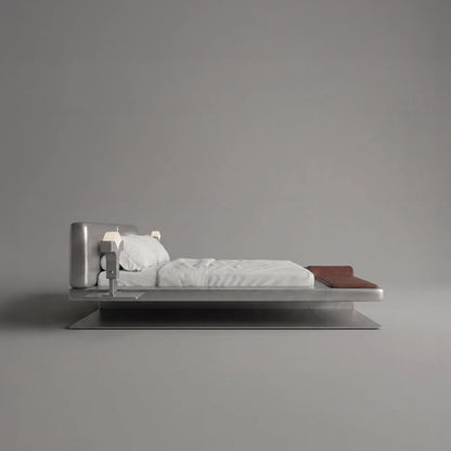 Side view of the Confluence bed by Diamant Versatile, with white bedding, brown leather details and a sculptural brushed metal frame.