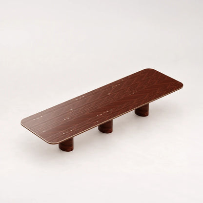 DT01 Dining Table from the X Collection by Eva Szumilas in reddish wood, with patterned grain, pale arrow inlays and three cylindrical supports.