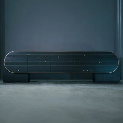 Full front view of the C01 Sideboard from the X Collection by Eva Szumilas, with an elongated rounded facade, gold-toned arrow details and two dark supports.