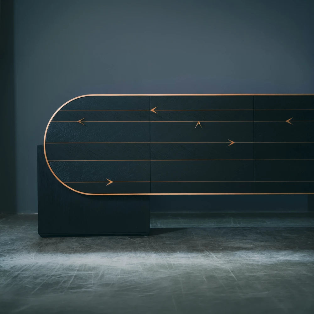 Partial front view of the C01 Sideboard by Eva Szumilas, highlighting its rounded left end, broad dark support and fine gold-toned lines.