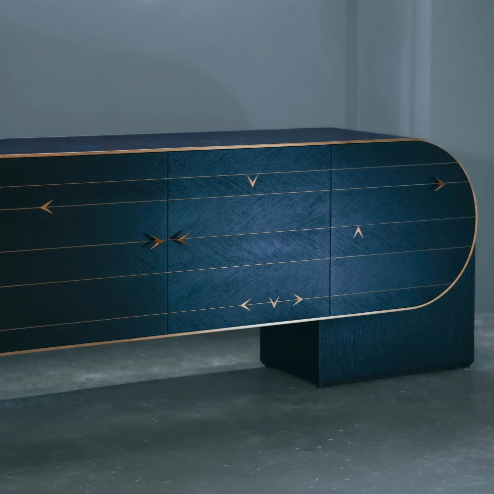 Right front detail of the C01 Sideboard by Eva Szumilas, with directional wood grain, gold-toned arrow motifs and horizontal inlays above a block support.