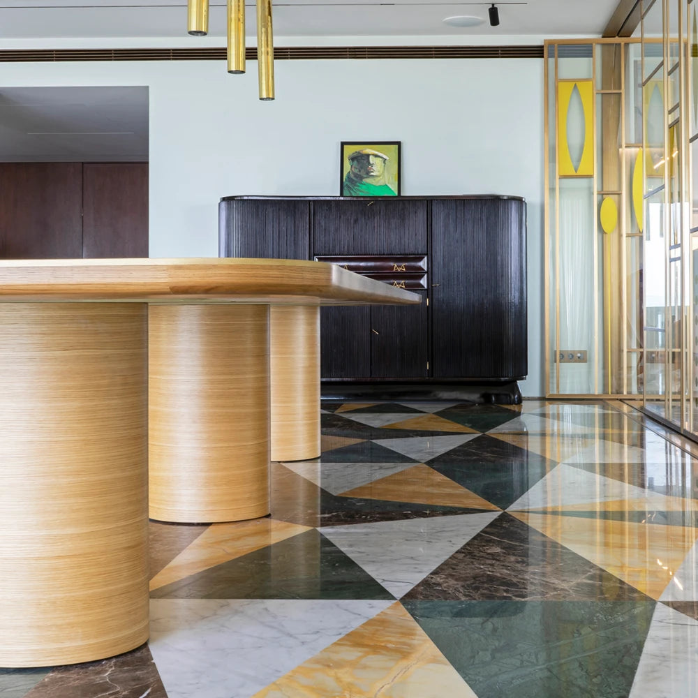 Low view beneath the oak DT01 Dining Table by Eva Szumilas, showing cylindrical wooden supports above a geometric marble floor in a furnished interior.