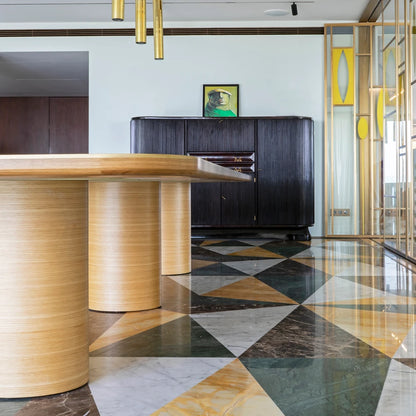 Low view beneath the oak DT01 Dining Table by Eva Szumilas, showing cylindrical wooden supports above a geometric marble floor in a furnished interior.