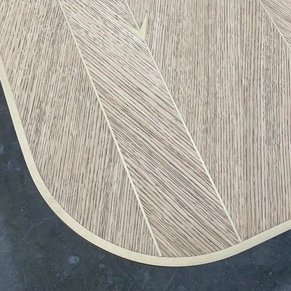 Overhead corner detail of the DT01 Dining Table by Eva Szumilas, highlighting contrasting oak grain directions, a gold-toned rim and an arrow inlay.