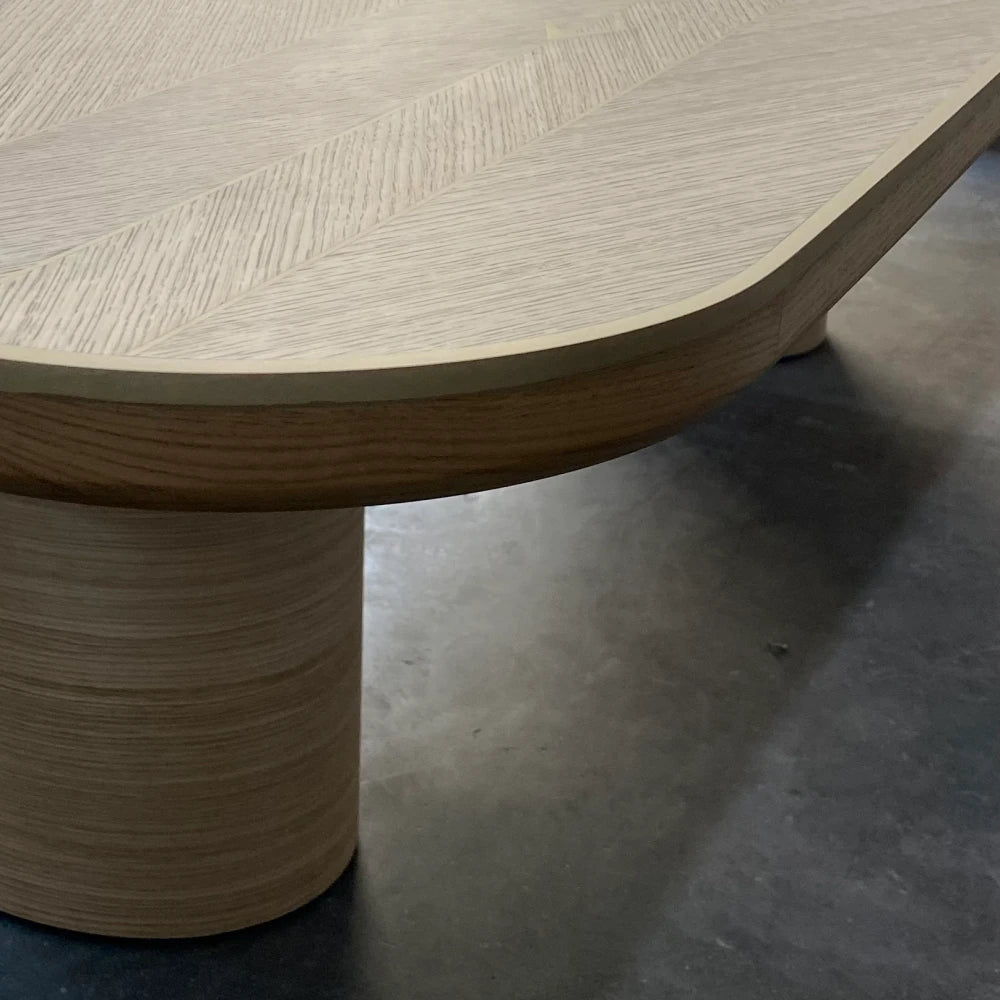 Edge detail of the oak DT01 Dining Table by Eva Szumilas, showing its rounded corner, gold-toned trim and cylindrical wooden support.