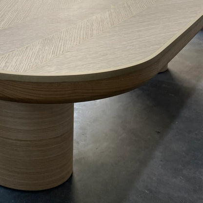 Edge detail of the oak DT01 Dining Table by Eva Szumilas, showing its rounded corner, gold-toned trim and cylindrical wooden support.