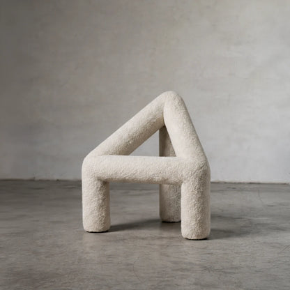 Three-quarter view of the white A Chair by Garnier Pingree on a concrete floor, showing its textured upholstery and open triangular frame.