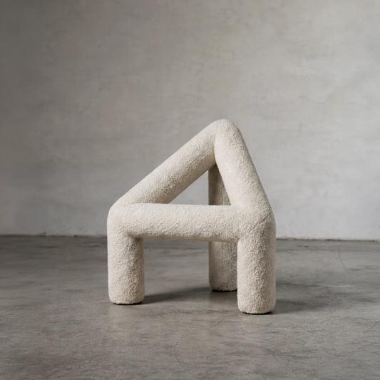Three-quarter view of the white A Chair by Garnier Pingree on a concrete floor, showing its textured upholstery and open triangular frame.