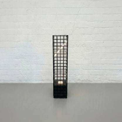 Front view of the black Ami Desk Lamp by Garnier Pingree, with a tall metal grid frame enclosing an angled illuminated panel.