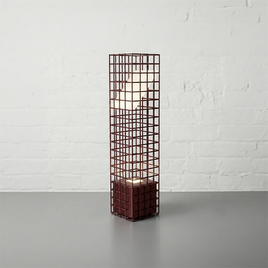 Three-quarter view of the maroon Ami Desk Lamp by Garnier Pingree, highlighting its slender metal grid structure and angled glowing panel.