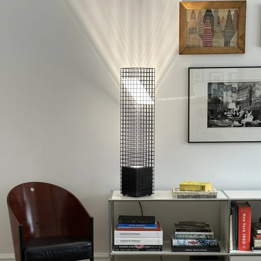 Illuminated Ami Table Lamp by Garnier Pingree on metal shelving beside books, casting a radiating grid pattern onto the wall.