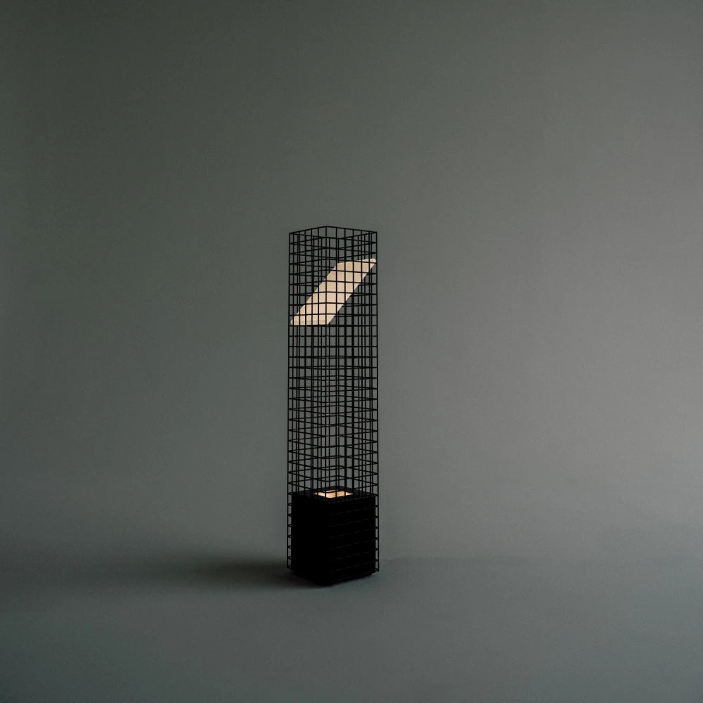 Three-quarter view of the illuminated black Ami Table Lamp by Garnier Pingree against a grey background, showing its grid frame and angled panel.