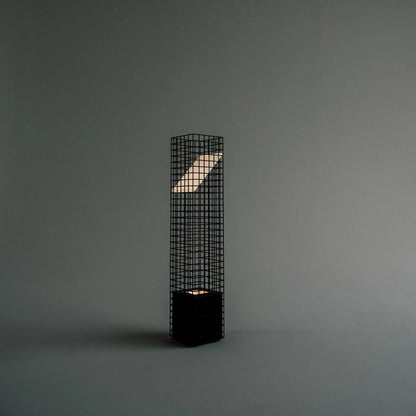 Three-quarter view of the illuminated black Ami Table Lamp by Garnier Pingree against a grey background, showing its grid frame and angled panel.