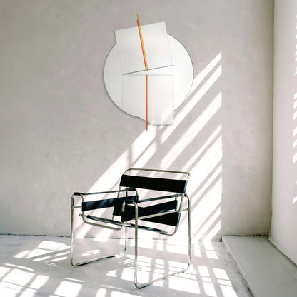 Large Claude Mirror by Garnier Pingree with red-orange and yellow rods, above a black tubular-frame armchair in an interior crossed by sunlight.