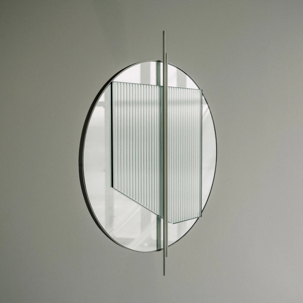Angled view of the small Claude Mirror by Garnier Pingree, with a circular mirror, ribbed glass panel and slender pale green vertical rods.