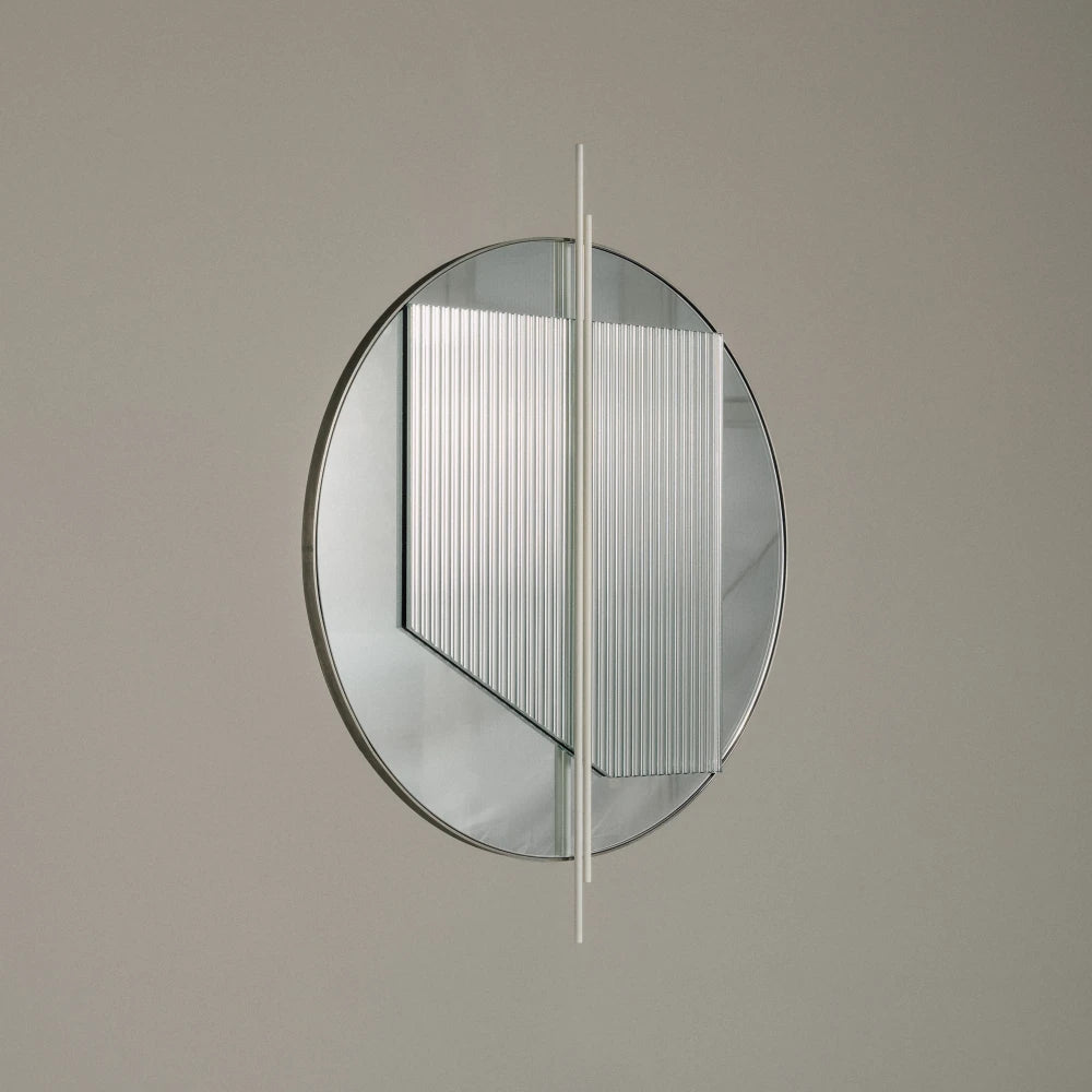 Small Claude Mirror by Garnier Pingree against a grey wall, showing its circular outline, overlapping ribbed glass panel and pale vertical rods.