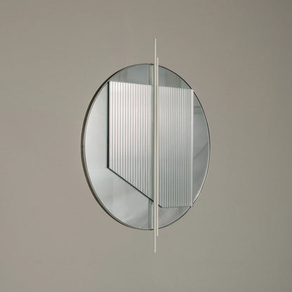 Small Claude Mirror by Garnier Pingree against a grey wall, showing its circular outline, overlapping ribbed glass panel and pale vertical rods.