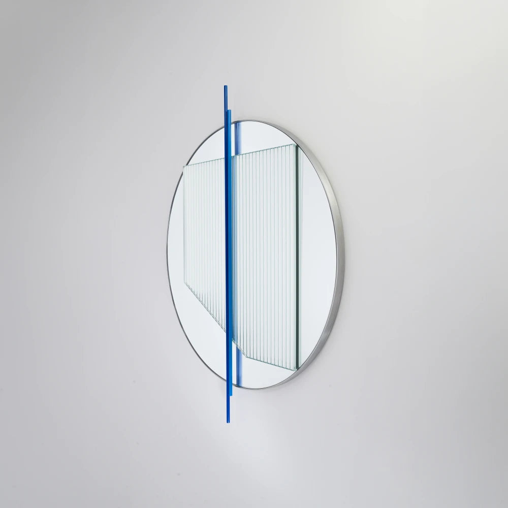 Angled view of the small Claude Mirror by Garnier Pingree, featuring blue vertical rods across a circular mirror and ribbed glass panel.