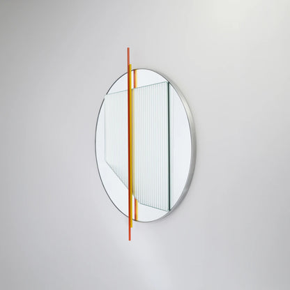 Angled view of the small Claude Mirror by Garnier Pingree, with red-orange and yellow rods crossing its circular mirror and ribbed glass panel.