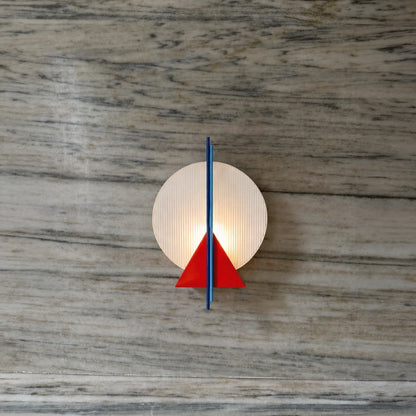 Front view of the Claude Wall Lamp by Garnier Pingree, combining a glowing ribbed glass disc, red triangular element and slender blue vertical rods.