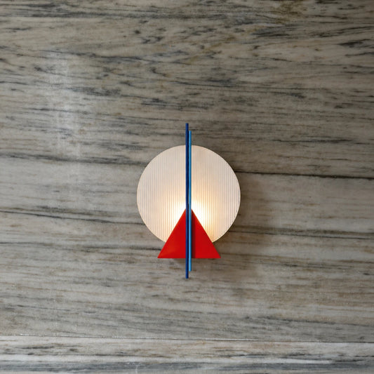 Front view of the Claude Wall Lamp by Garnier Pingree, combining a glowing ribbed glass disc, red triangular element and slender blue vertical rods.