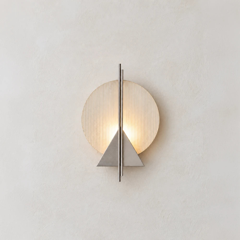 Illuminated Claude Wall Lamp by Garnier Pingree on a textured white wall, showing its circular ribbed glass and brushed stainless steel details.