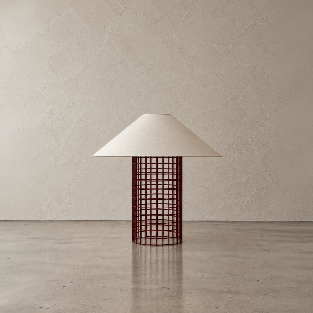 Maroon Ento Table Lamp by Garnier Pingree, with a slender cylindrical grid base and cream conical shade against a textured beige wall.