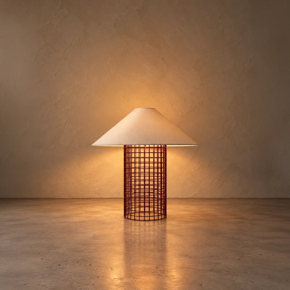 Illuminated maroon Ento Table Lamp by Garnier Pingree, casting warm light through its grid base and cream shade onto the wall and surface.