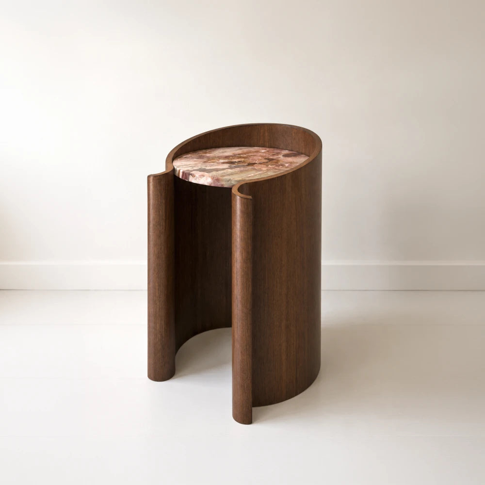 Closer view of the Volute Side Table by Garnier Pingree, highlighting its rounded wooden scrolls, open front and pink-and-brown stone tabletop.